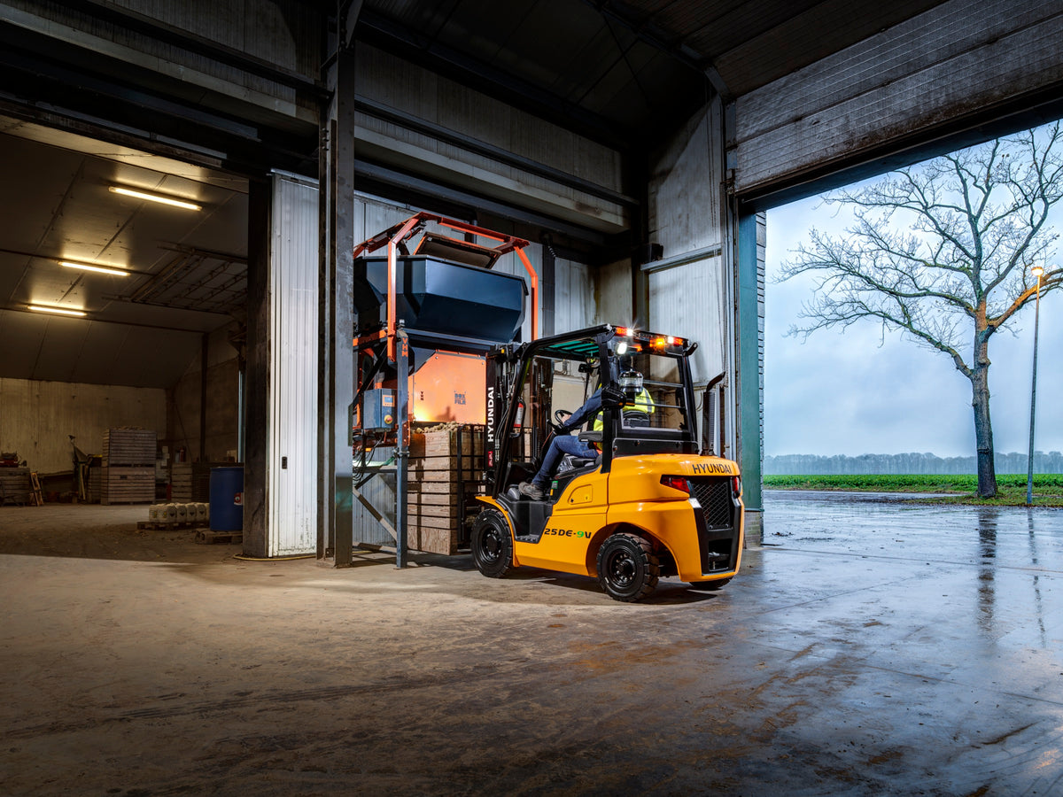 Hyundai 25DE-9V gaffeltruck kører ud af en lagerport i regnvejr